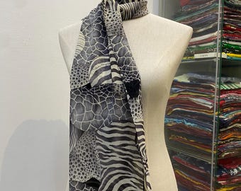 May include: A rectangular silk scarf featuring a monochromatic black and white animal print pattern with sections of zebra stripes, giraffe spots, and leopard dots. The scarf is draped around a mannequin neck and includes the Salvatore Ferragamo logo.