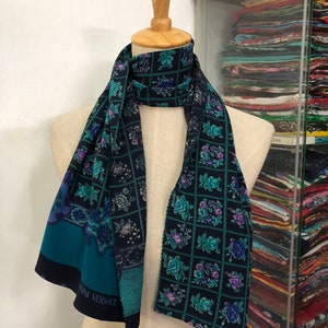 May include: A teal and black silk scarf with a floral pattern and the text "ANN VERSACE" printed on the bottom edge.