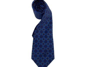 May include: A rolled-up navy blue tie with a repeating geometric pattern in shades of blue and gold. The tie is made of a smooth fabric and is suitable for formal occasions.
