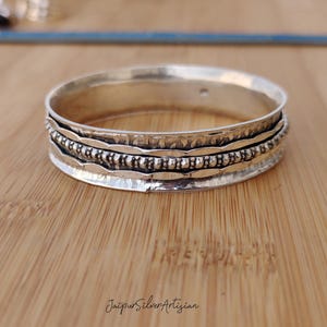 May include: A silver bangle bracelet with a hammered finish and a beaded design. The bracelet is made of sterling silver and is approximately 2 inches in diameter.