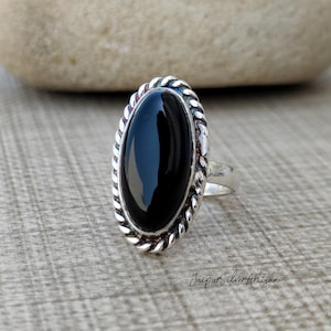 Op de afbeelding: Een zilveren ring met een zwarte ovale onyx-edelsteen, gezet in een touwachtige rand.