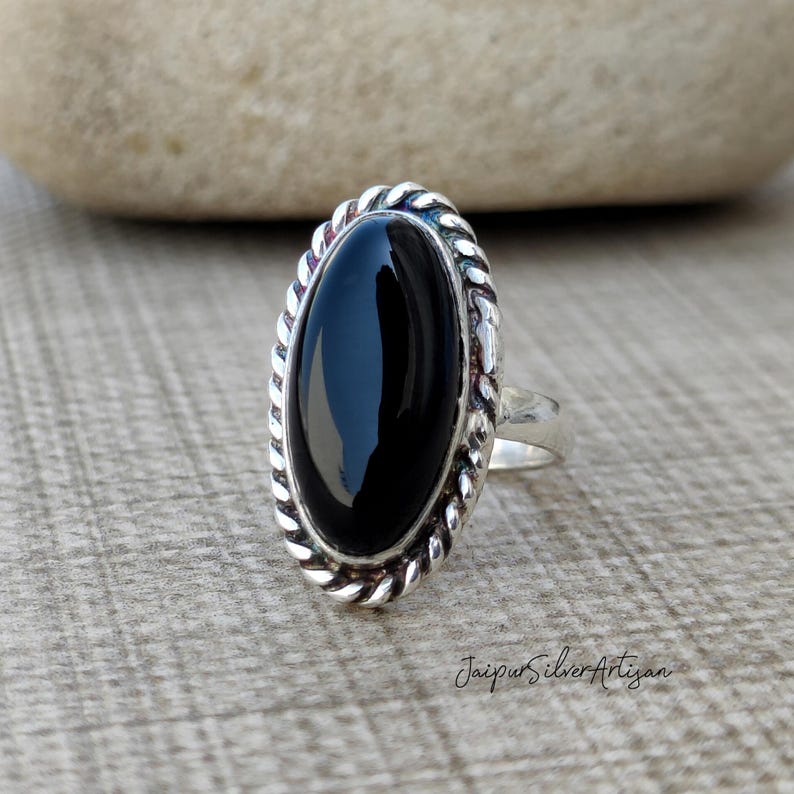 Op de afbeelding: Een zilveren ring met een zwarte ovale onyx-edelsteen, gezet in een touwachtige rand.