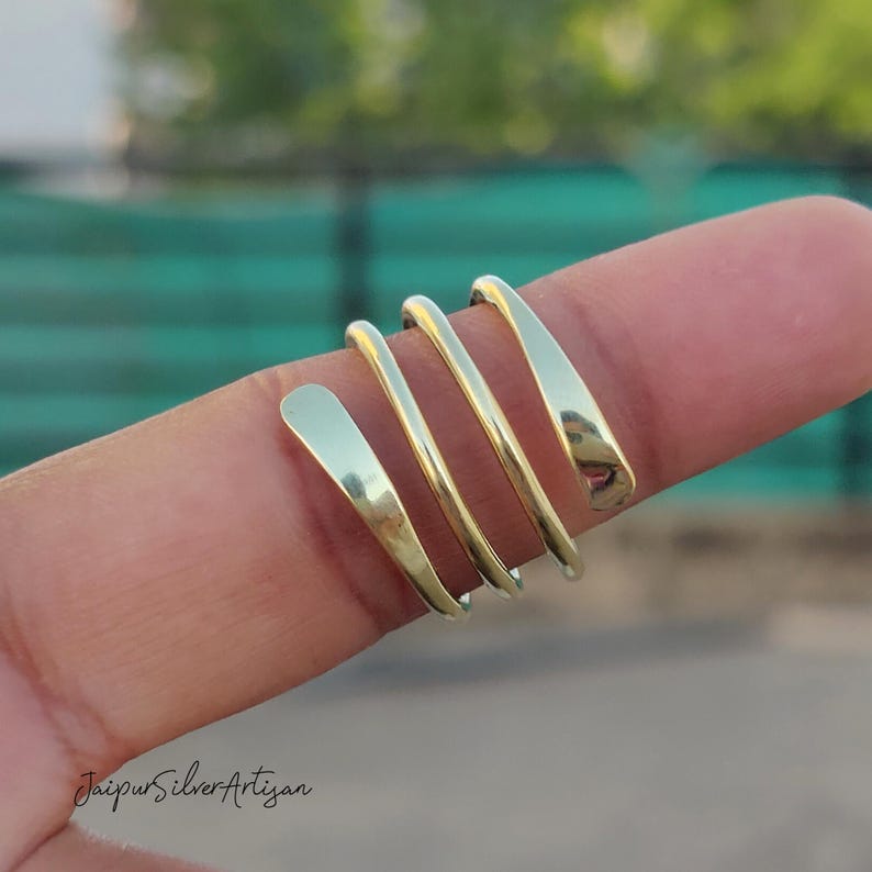 May include: A gold-coloured spiral ring made of multiple thin bands of metal. The ring is worn on a finger.