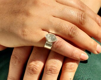 May include: A silver ring with a clear, faceted gemstone set in a heart-shaped bezel. The ring is on a person's finger.