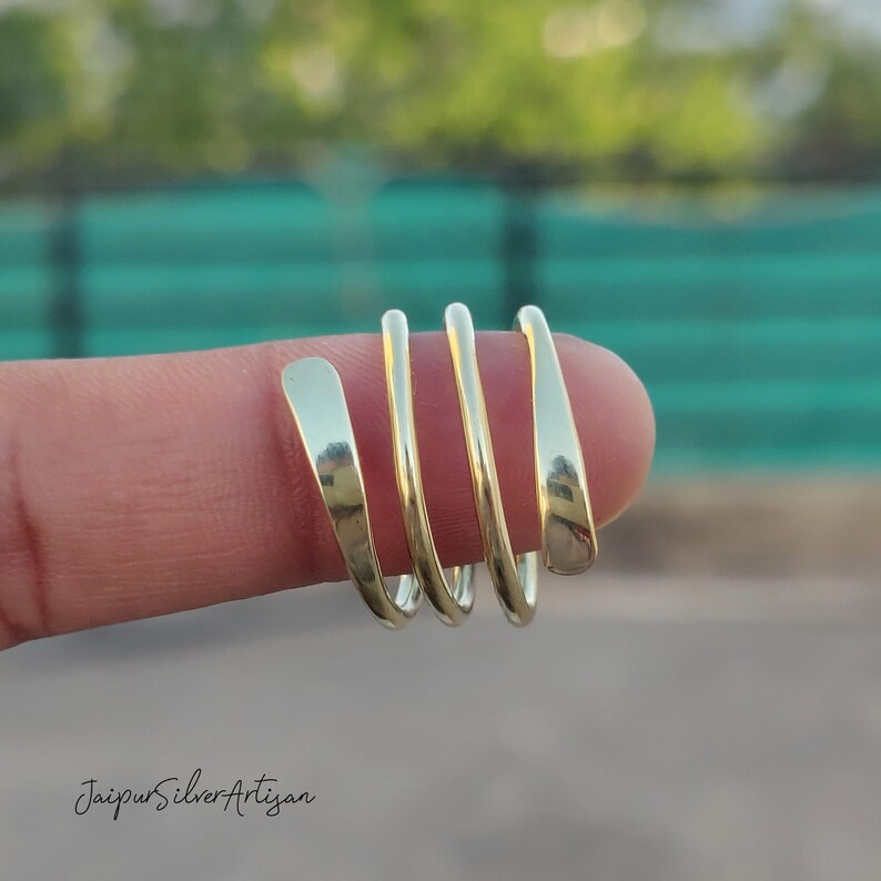 May include: A gold-coloured, multi-strand ring with a unique, twisted design. The ring is worn on a finger.