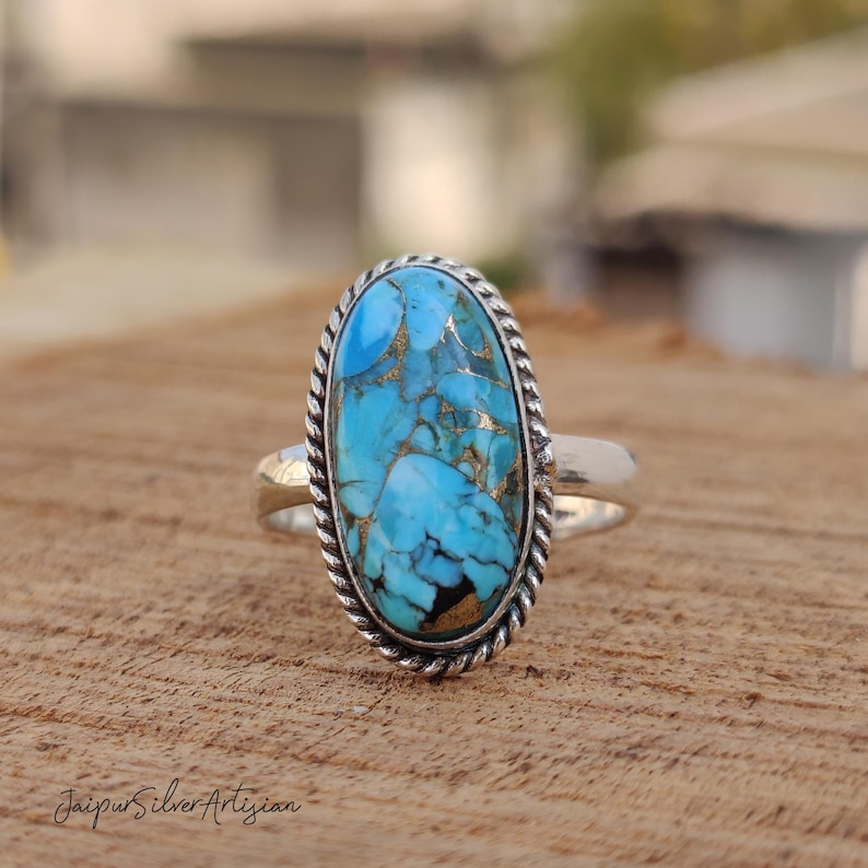 Op de afbeelding: Een zilveren ring met een ovale, blauwe en gouden turquoise steen, gezet in een band met touwdesign.