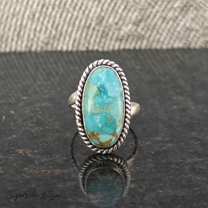 Op de afbeelding: Een zilveren ring met een ovale turquoise steen gezet in een touwachtige rand.