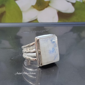 May include: A silver ring with a rectangular moonstone set in a bezel setting. The ring has a triple band design.