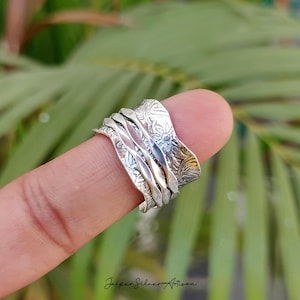 Peut inclure: Une bague en argent avec un motif floral et gravé. La bague comporte plusieurs bandes rotatives. La bague est portée sur un doigt. Le texte "Jaipur Silver Artisan" est au bas de l'image.