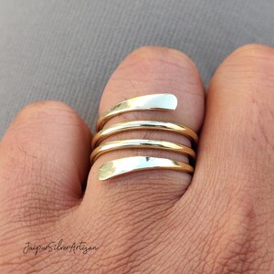 May include: A gold and silver spiral ring with multiple bands. The ring is worn on a finger.