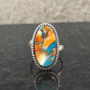 Op de afbeelding: Een zilveren ring met een ovale turquoise steen. De steen is een mix van oranje, blauwe en witte kleuren.