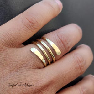 May include: A gold-toned, spiral-shaped ring with four bands. The ring is worn on a person's finger.