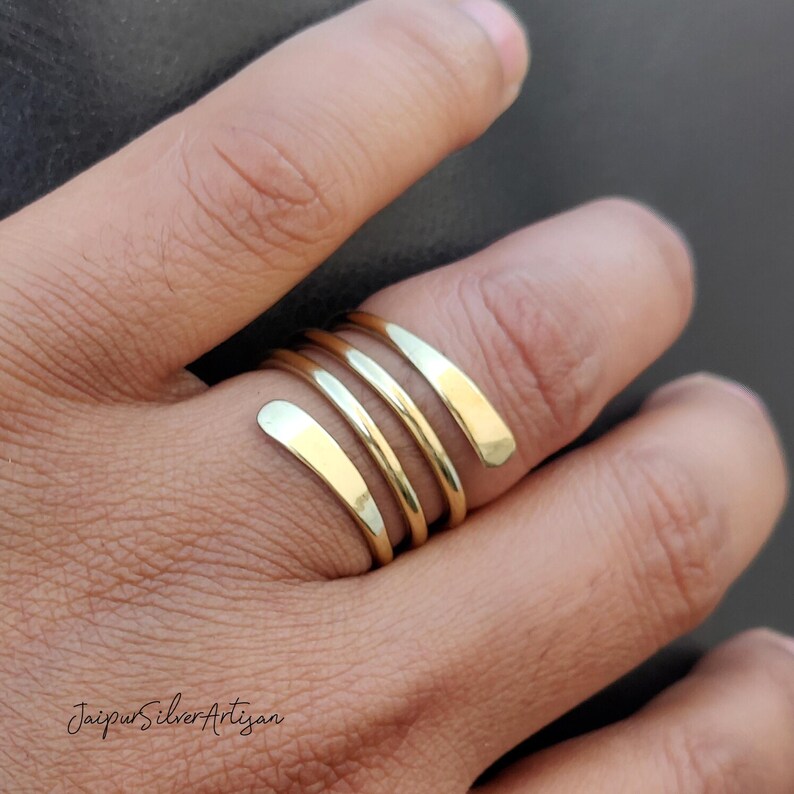 May include: A gold-toned, spiral-shaped ring with four bands. The ring is worn on a person's finger.