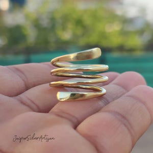 May include: A gold-toned spiral ring made of twisted metal. The ring is thick and has a smooth, polished finish.