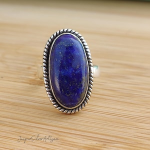 Op de afbeelding: Een zilveren ring met een grote ovale lapis lazuli-edelsteen. De ring heeft een touwachtig ontwerp rond de rand van de zetting.