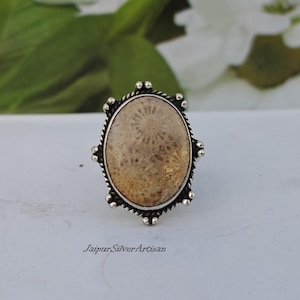 May include: A silver ring featuring a fossilized coral stone set in an oval bezel. The ring has a decorative border with small silver beads.