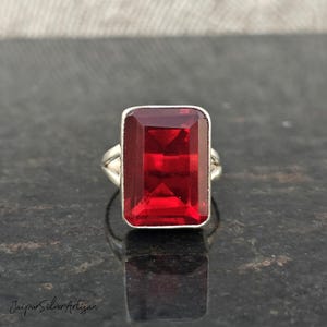 Peut inclure: Une bague en argent avec une grande pierre précieuse rectangulaire rouge. La bague est sertie dans un style simple et élégant.