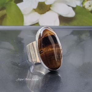 May include: A silver ring featuring an oval tiger's eye gemstone. The ring has a textured band and the gemstone displays brown and gold stripes.