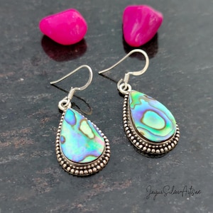 May include: A pair of silver dangle earrings with iridescent abalone shell teardrop-shaped pendants. The earrings have a beaded border around the shell.