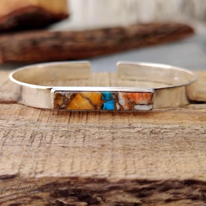 May include: A silver cuff bracelet with a rectangular inlay of multi-colored turquoise and orange stones.