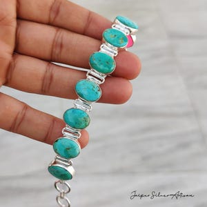 May include: A silver bracelet featuring oval turquoise stones. The turquoise stones are set in a silver link chain. The bracelet is held in a hand, showcasing the jewelry's design and color. The bracelet is a piece of artisan jewelry.