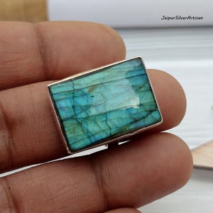 May include: A silver ring featuring a large, rectangular, iridescent blue labradorite gemstone.