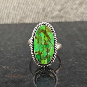 Op de afbeelding: Een zilveren ring met een groene ovale turquoise steen gezet in een band met touwontwerp.