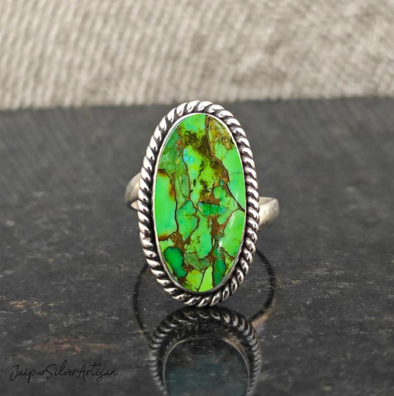 Op de afbeelding: Een zilveren ring met een groene ovale turquoise steen gezet in een band met touwontwerp.