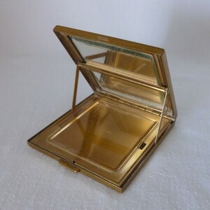 May include: A gold-toned metal compact with a hinged mirror. The compact is open, revealing a gold-toned interior.
