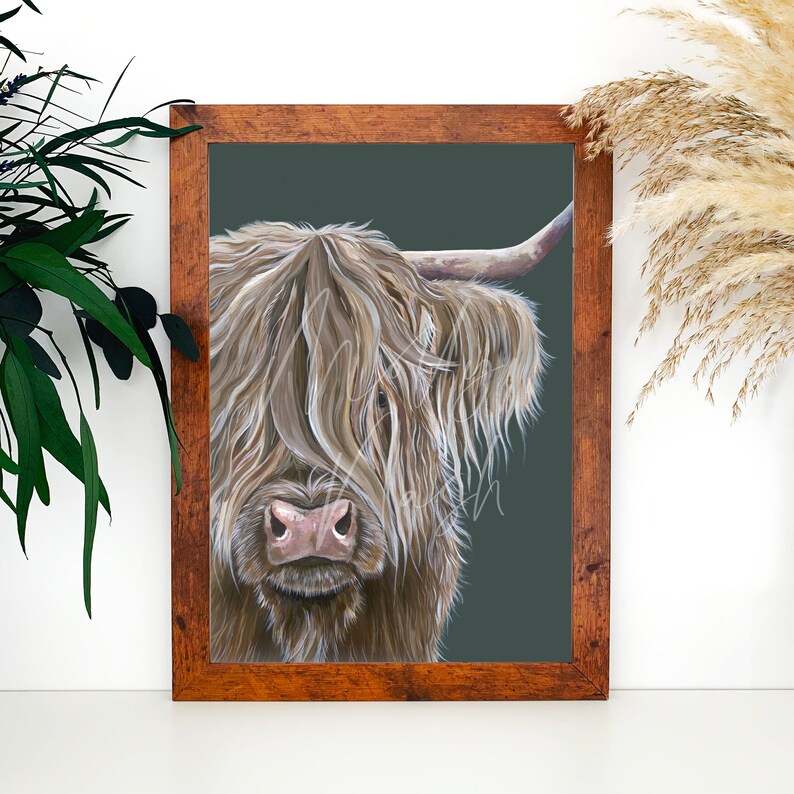 May include: A framed print of a Highland cow with long, shaggy brown fur. The cow's face is partially obscured by its fur, and its pink nose is visible. The background is a dark teal colour.