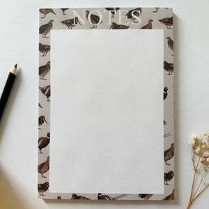 May include: A white notepad with a border of brown and white birds. The word "NOTES" is printed in white at the top of the notepad.