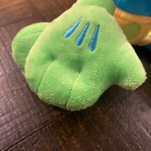 Op de afbeelding: Een groene pluche hand met drie blauwe steken op de achterkant van de hand.