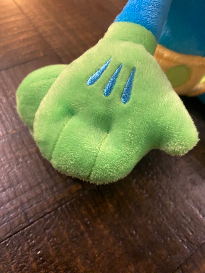 Op de afbeelding: Een groene pluche hand met drie blauwe steken op de achterkant van de hand.