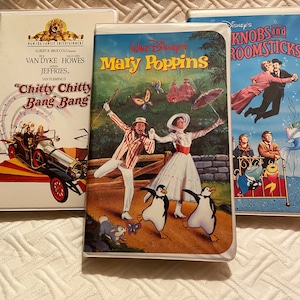 May include: Three VHS tapes, one with a blue background and the text "Disney's Knobs and Roomsticks", one with a green background and the text "Walt Disney's Mary Poppins", and one with a white background and the text "MGM/UA Family Entertainment Albert R. Broccoli Presents Van Dyke Howes Ian Fleming's "Chitty Chitty Bang Bang"