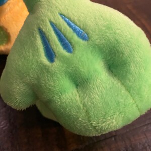 Op de afbeelding: Close-up van een groene pluche hand met drie blauwe geborduurde lijnen op de palm.