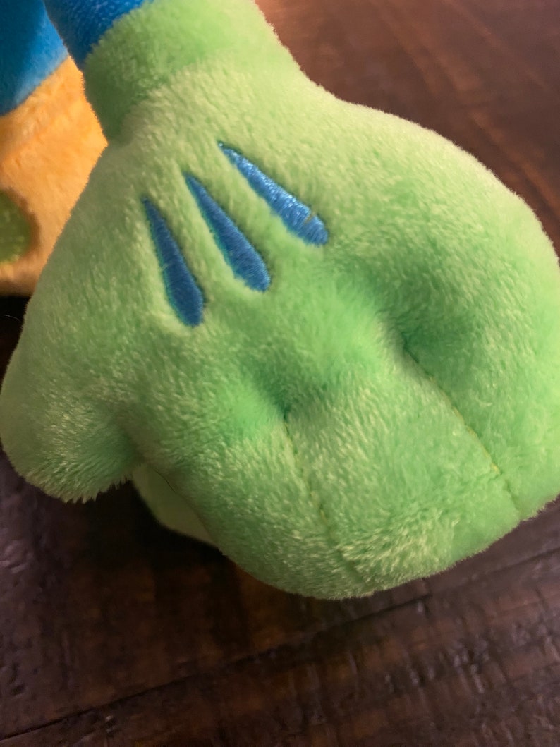 Op de afbeelding: Close-up van een groene pluche hand met drie blauwe geborduurde lijnen op de palm.