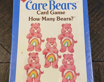 May include: A blue and white box for a Care Bears card game. The box features a picture of five Care Bears with rainbow bellies. The text on the box reads "Care Bears Card Game How Many Bears?"