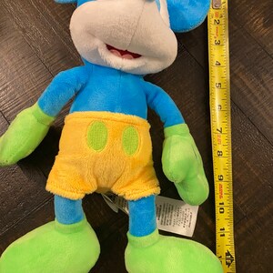 Op de afbeelding: Blauw en geel pluche Mickey Mouse speelgoed met groene schoenen en een label op de voet. Het speelgoed is ongeveer 28 cm hoog.