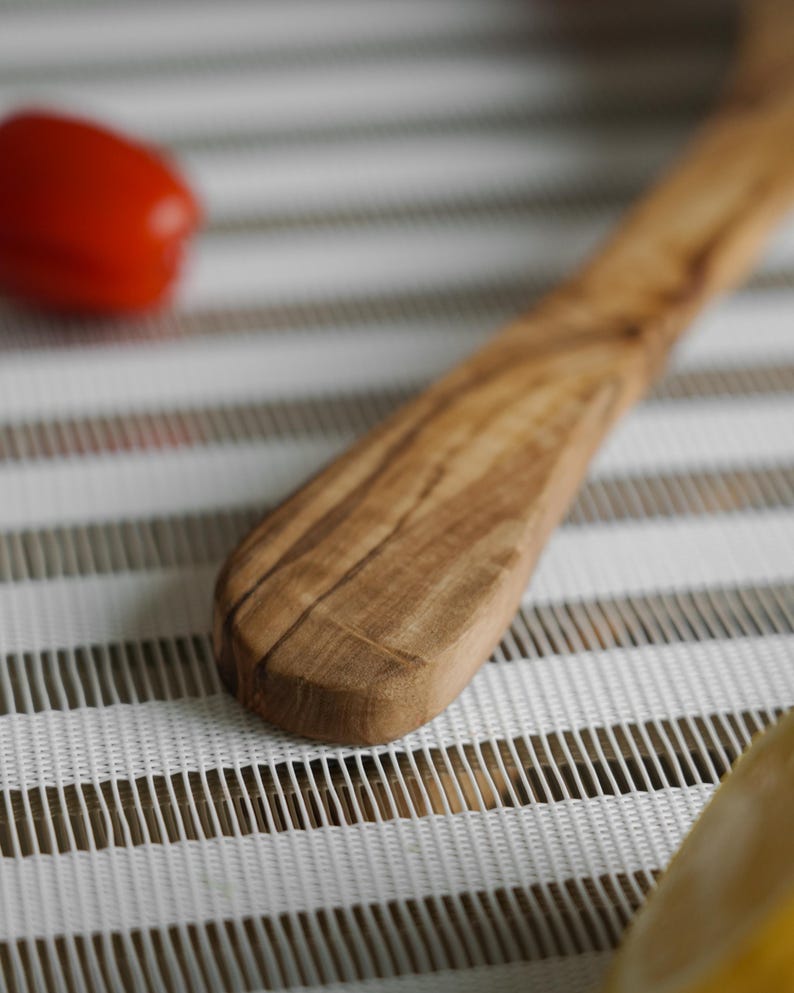 Puede incluir: Primer plano de un cuchillo de mantequilla de madera con un patr&oacute;n de veta de madera natural. El cuchillo est&aacute; sobre una superficie rayada blanca y marr&oacute;n.
