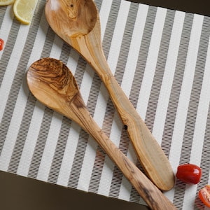 May include: Two wooden cooking spoons with a distinct natural grain pattern and light brown color. The spoons feature smooth, rounded bowls and long, sturdy handles, showcasing the organic texture and variations of the wood material.