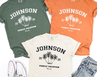 Può includere: Tre magliette a maniche corte in verde oliva, arancione e crema. Ogni maglietta presenta il testo JOHNSON, 20 26, FAMILY VACATION e Florida, insieme a una grafica di tre palme. Sono inclusi un paio di scarpe da ginnastica bianche e jeans blu.