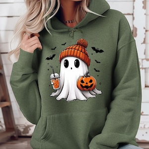 Pu&ograve; includere: Felpa con cappuccio verde oliva con un fantasma dei cartoni animati che indossa un berretto arancione e tiene in mano una bevanda alle spezie di zucca e una zucca di Halloween. Pipistrelli neri sono sparsi intorno al fantasma. Un divertente design a tema Halloween.