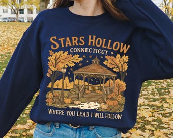 May include: Navy blue sweatshirt with a graphic featuring a gazebo, pumpkins, and fall foliage. The text reads "Stars Hollow Connecticut" and "Where you lead I will follow". A cozy autumn-themed design.