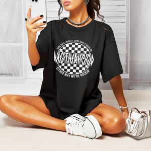 May include: Black oversized t-shirt with a white graphic print of a checkered circle with the text "SOME DAYS I ROCK IT. SOME DAYS IT ROCKS ME. MOTHERHOOD. EITHER WAY WE'RE ROCKIN'"