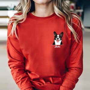 May include: A long-sleeved red shirt featuring a graphic of a dog with black and white markings and the name "Bella" underneath. The dog graphic is on the left chest area of the shirt.