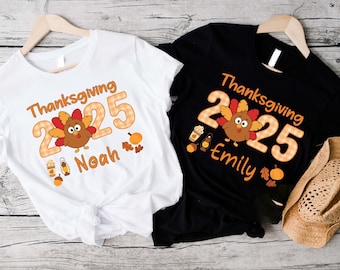 May include: Two t-shirts, one white and one black, each featuring a Thanksgiving design. The design includes the text "Thanksgiving 2025", a cartoon turkey, and a name. The white shirt says "Noah", and the black shirt says "Emily".