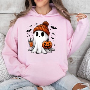 Pu&ograve; includere: Felpa con cappuccio rosa chiaro con un fantasma dei cartoni animati con un berretto arancione, una zucca e una bevanda. Pipistrelli e stelle nere circondano il fantasma, creando un tema di Halloween.