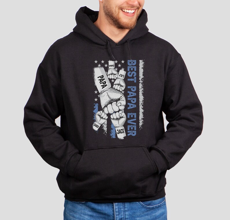 May include: Black hooded sweatshirt with a graphic of fists with names on the knuckles, including "Papa", "Jack", "Jax", and "Sadie". The graphic is set against a blue and white American flag design. The text "Best Papa Ever" is printed vertically on the right side of the graphic.