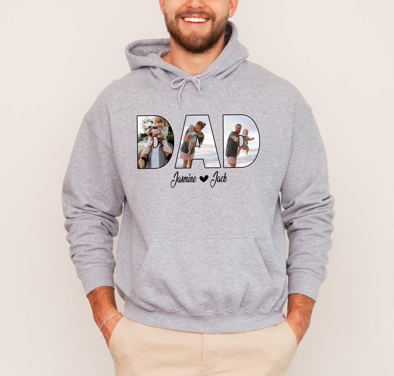 May include: A grey hooded sweatshirt with the word "DAD" printed on the front. The letters are filled with photos of a father and his children. The text "Jasmine &hearts; Jack" is printed below the word "DAD".