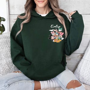 May include: A dark green hooded sweatshirt with a pocket and a graphic of Mickey Mouse and friends. The text "Emily" is printed on the sweatshirt.